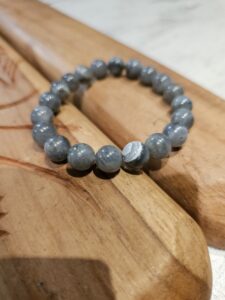 Bracelet élastique de perles gris bleu clair posées sur une surface en bois.