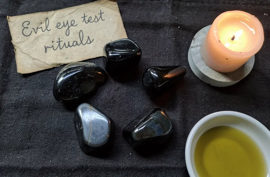 Pierres d'obsidienne noire posées sur un tissu sombre à côté d'une bougie et d'un bol d'huile d'olive pour un rituel de détection du mauvais œil.