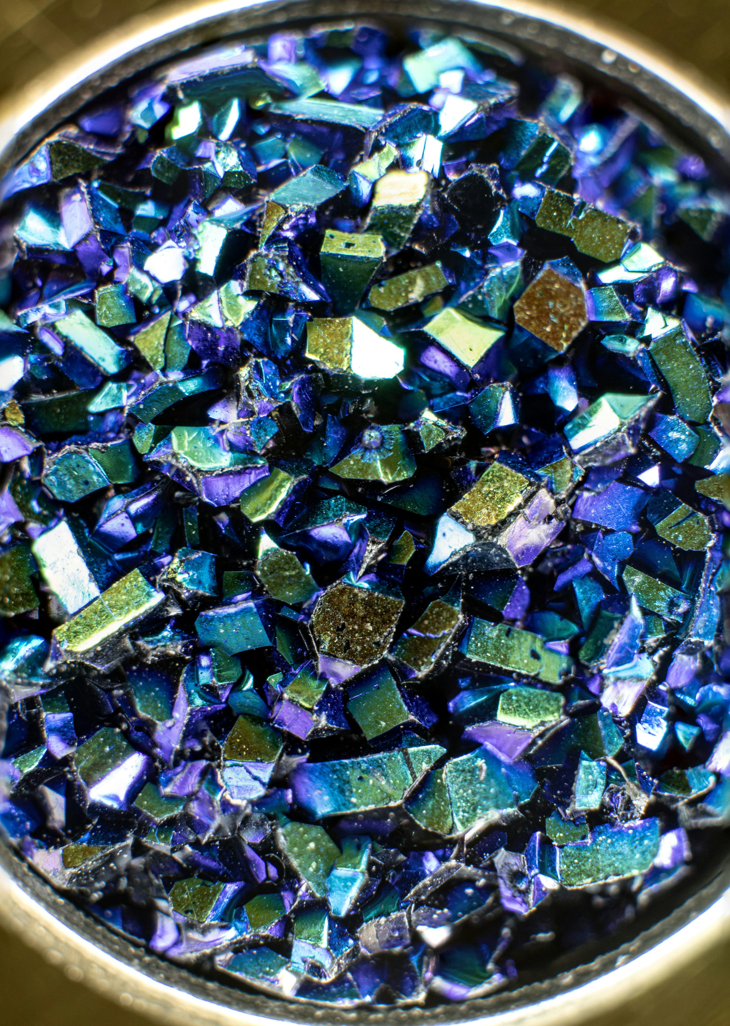 Poudre scintillante bleu-vert avec fragments métalliques multicolores, posé dans un récipient rond.